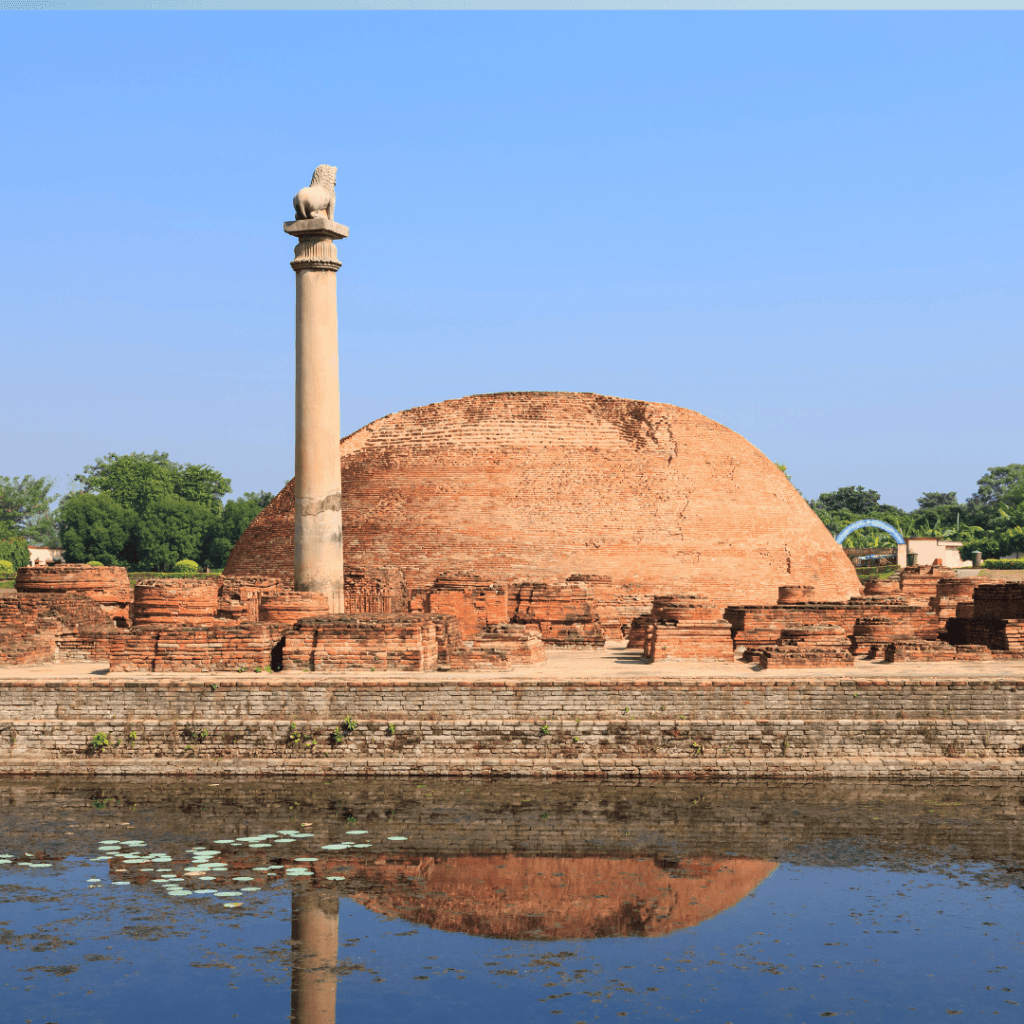"The ancient sandstone Ashokan Pillar at Vaishali, topped with a single seated lion capital, standing before a brick stupa under a clear sky."